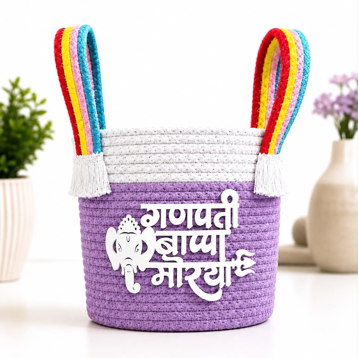 Lavender braided cotton rope basket with white rope band, rainbow handles with white tassels and white Ganpati Bappa Morya lettering.
